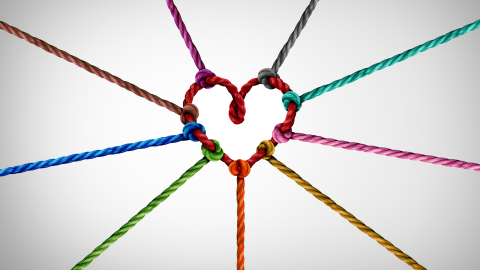 A knit heart stitched with multi-colored yarn stands against a white background.