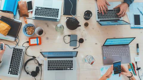 A group of people sit around a table using their digital devices. Courtesy of Unsplash.
