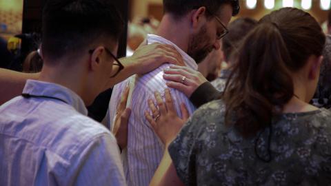 Image of a group of people praying over a ministerial candidate at Synod 2026. Courtesy of the Office of the General Secretary.
