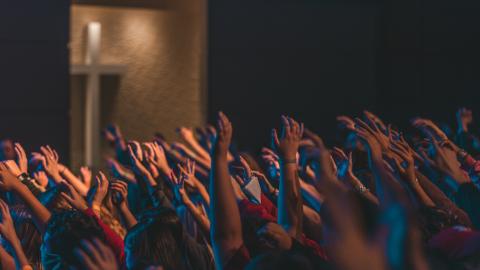 A group of people all raise their hands together in worship. Courtesy of Unsplash.