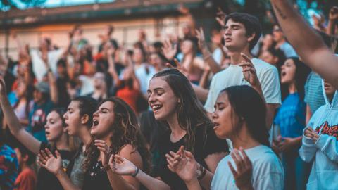 A group of young adults are gathered together in worship with their hands raised. Courtesy of Pexels.