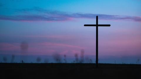 A cross stands against a sunset background. Courtesy of Unsplash.