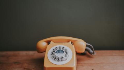 An orange handheld phone sits on a wooden table. Courtesy of Unsplash.