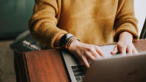 Someone sits at a desk, typing on a computer as they work. Courtesy of Chritian Hume on Unsplash.