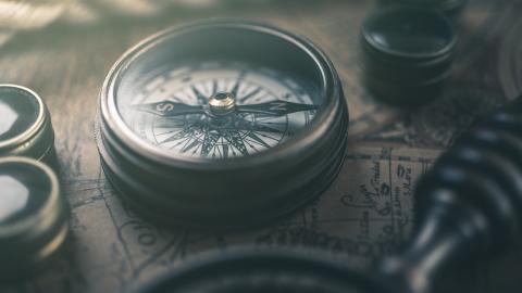 A directional compass sits on a map next to a magnifying glass.