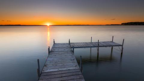 A pier reaches out into a lake. Courtesy of Unsplash.