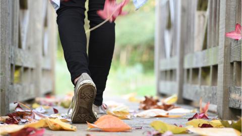 Photo of someone's feet walking along a path with falling leaves