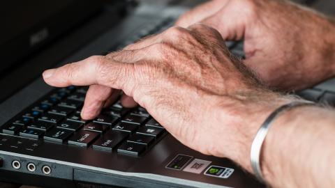 wrinkled hands type on a laptop keyboard
