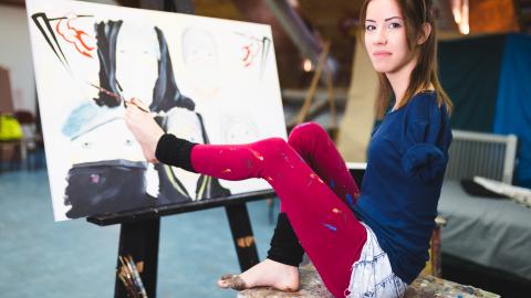 woman artist using her feet to paint, sitting infront of a painting on a canvas