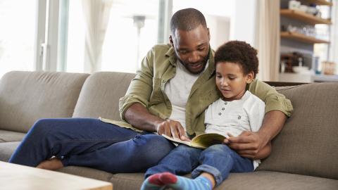 a father and son read a book together on a couch
