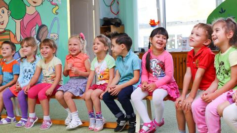 A group of kids stands together smilling while looking at a teacher. Courtesy of Pexels.