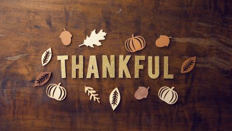 Words "thankful" are included against a wooden background with small decoration of pumpkins and fall leaves.