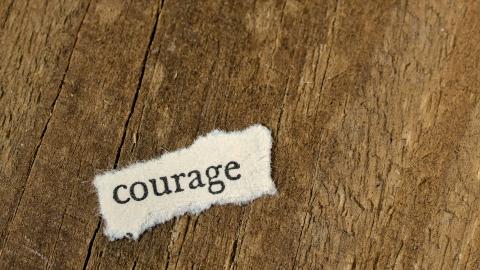 A small piece of paper sits against a wooden board, with the word "courage" written on it.