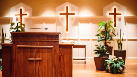 Preacher's pulpit stands in the foreground, with three crosses in the background against a lit wall.