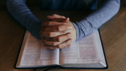 An individual holds their hands open over their bible in prayer. Courtesy of Patrick Fore on Unsplash.