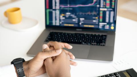 Praying hands in front of a laptop showing stock graphs.