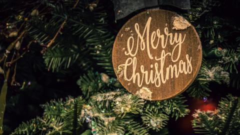 A plaque that reads "Merry Christmas" sits on an evergreen tree. Courtesy of Brett Sayles on Pexels.