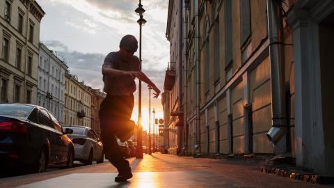A man dances in a busy street while the sun sets in the background