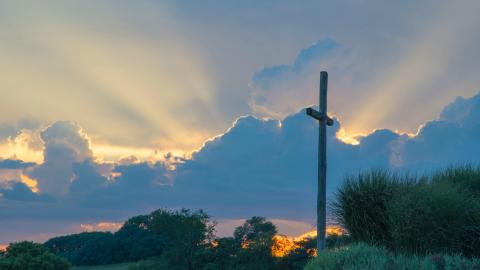 On a background of a setting sun, a cross stands on a hill