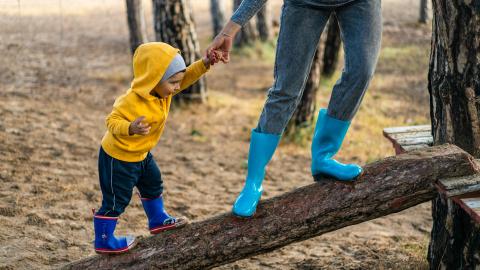 A child walks up a log, guided by their parent.
