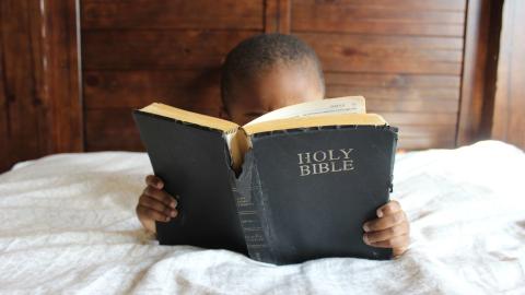 Child reads the Bible in bed