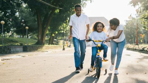 A girl is riding a bike, followed by her father and mother. Courtesy of Agung Pandit Wanga on Pexels.