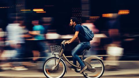 A man on a bicycle rides through a busy city street.