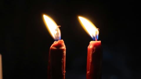 Two candles burn against a black background.