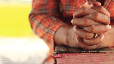 Hands clasped in prayer rest on a worn Bible