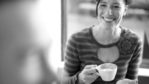 A woman sits and drinks a cup of coffee.