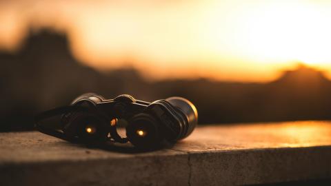 A pair of binoculars sits on a fence. Courtesy of Unsplash. 