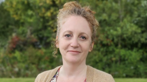 Becky Jones headshot, with Becky wearing her hair in a bun, with a light brown cardigan and floral shirt