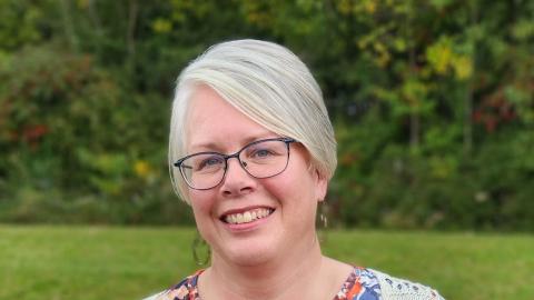 Photograph of Trudy Ash, wearing a colorful floral shirt on a background of a green lawn.