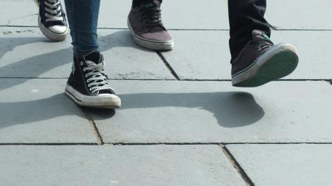 two pairs of feet stroll next to each other on a paved walkway