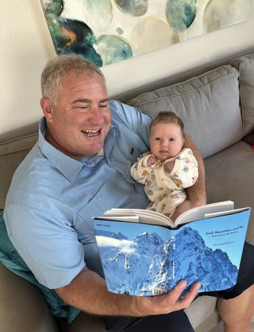 Rev. Tim Rietkirk sits holding his baby granddaughter and his mother's book.